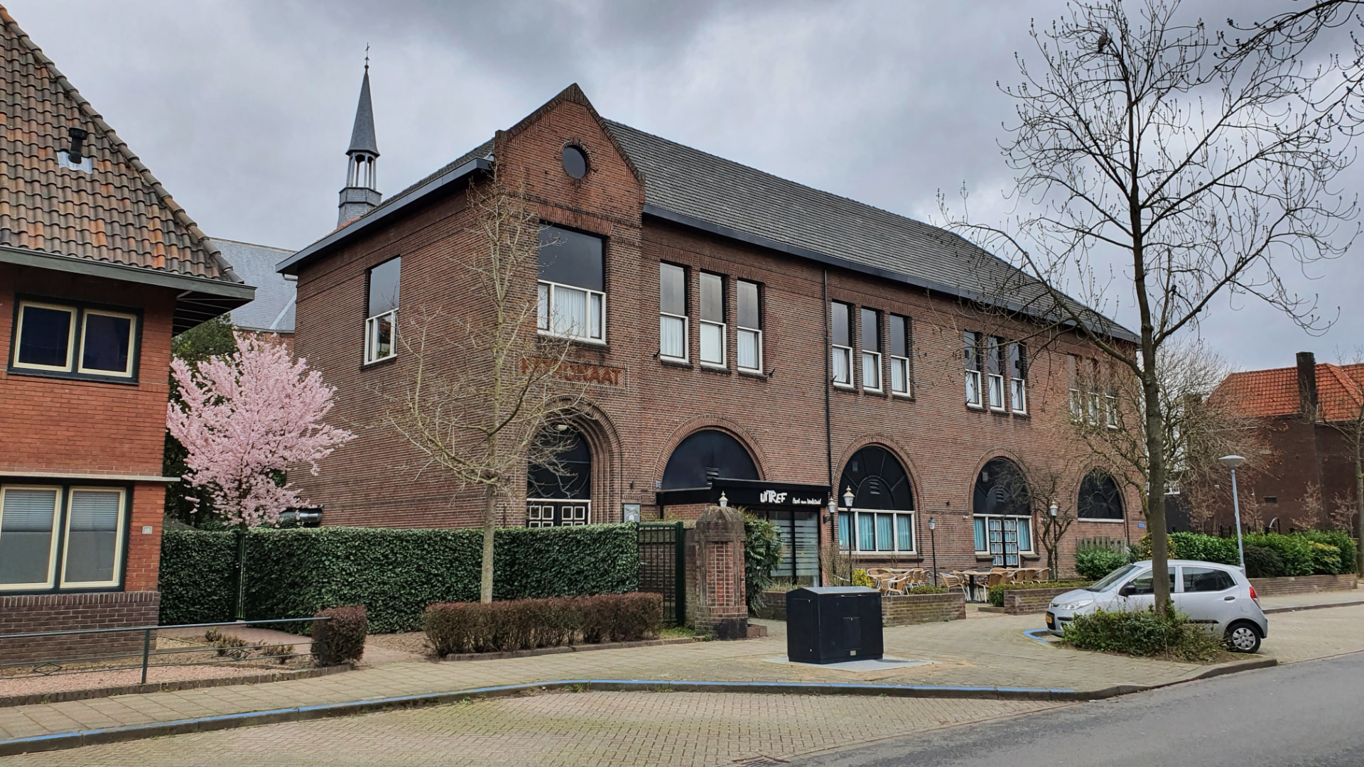 Ut Tref in Venlo-Zuid: een historisch bakstenen gebouw met hoge boogvensters, entreebord en een kerktoren op de achtergrond