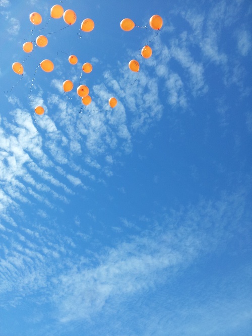 Oranje ballonnen die opstijgen tegen een blauwe lucht