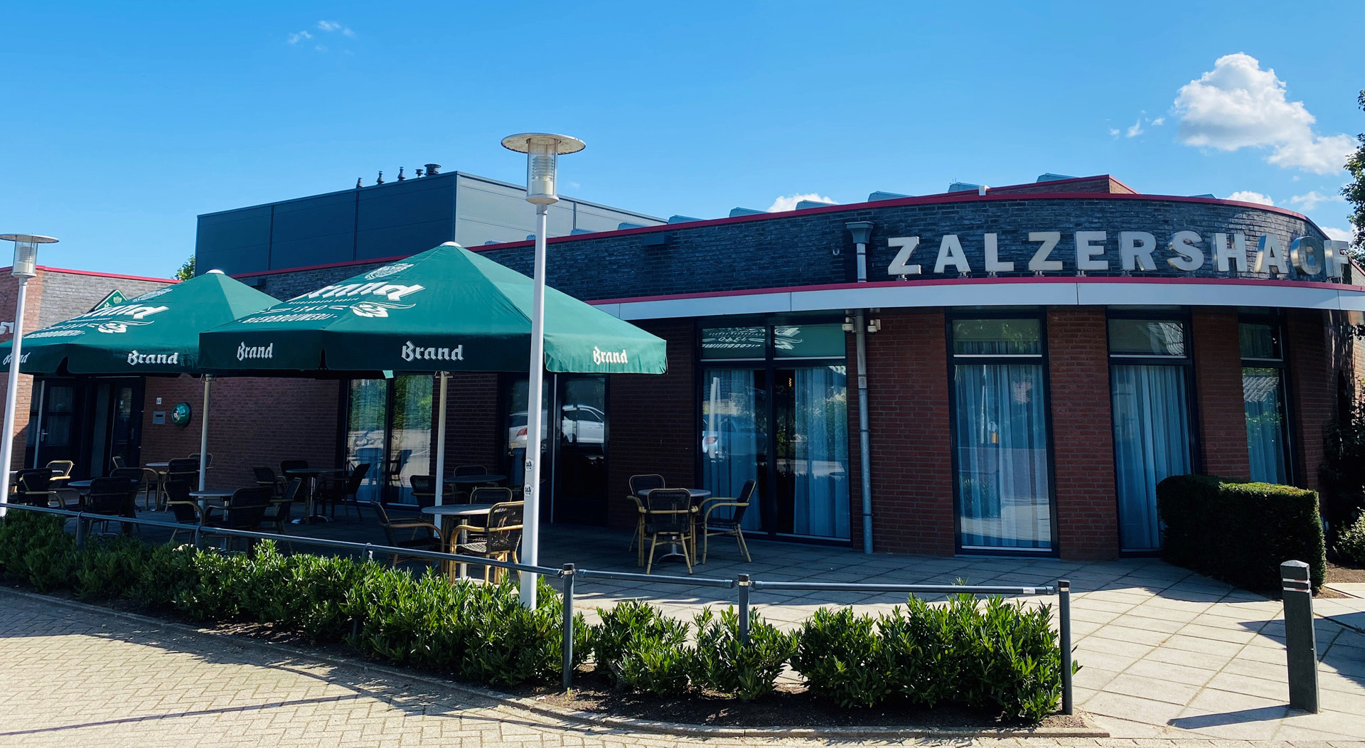 Het terras van Zalzershaof in Hout-Blerick, met groene parasols, tafels en de naam van het gebouw op de gevel